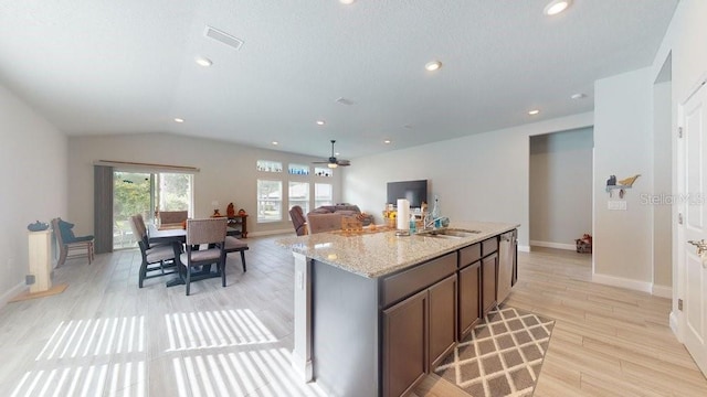 kitchen with light stone countertops, light wood-type flooring, vaulted ceiling, ceiling fan, and a center island with sink