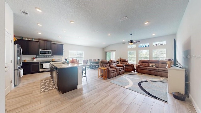 kitchen featuring a breakfast bar area, ceiling fan, an island with sink, light stone counters, and stainless steel appliances