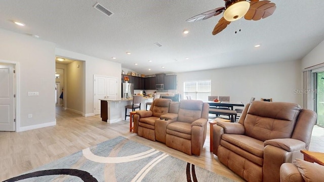 living room featuring ceiling fan, light wood-type flooring, a textured ceiling, and lofted ceiling