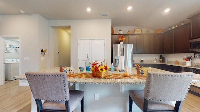 kitchen with washer / dryer, dark brown cabinetry, appliances with stainless steel finishes, and a kitchen island with sink