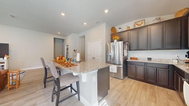 kitchen featuring a center island, stainless steel fridge, light stone countertops, and light hardwood / wood-style flooring