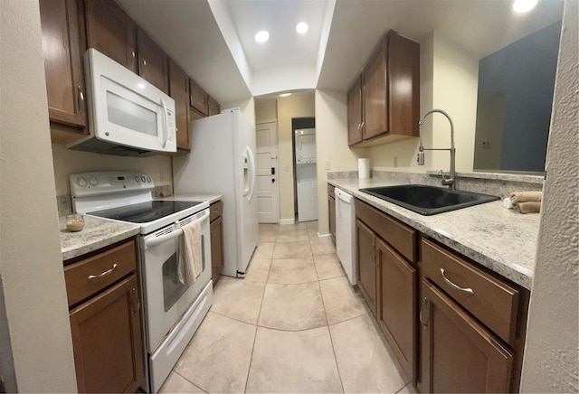 kitchen with light stone countertops, dark brown cabinets, white appliances, sink, and light tile patterned floors