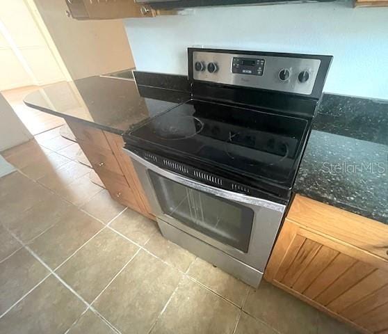 kitchen featuring dark stone counters, light tile patterned floors, and stainless steel electric range oven