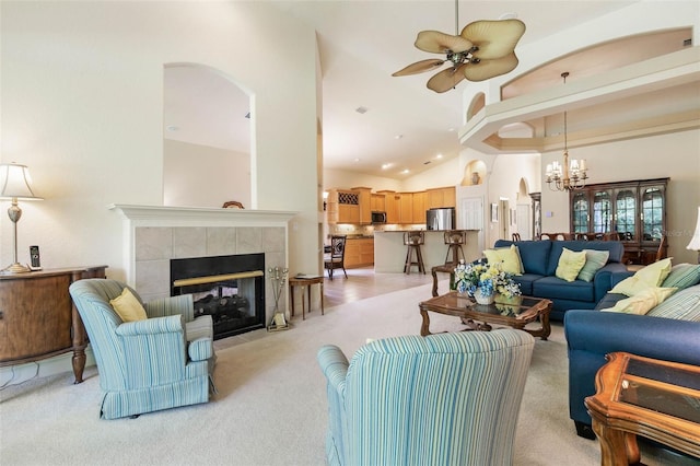 living room featuring light carpet, high vaulted ceiling, a fireplace, and ceiling fan with notable chandelier