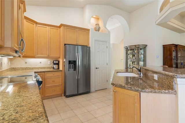 kitchen with tasteful backsplash, stone counters, light tile flooring, stainless steel refrigerator with ice dispenser, and sink