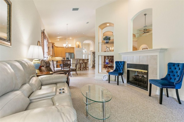 living room with ceiling fan with notable chandelier, high vaulted ceiling, light carpet, and a tiled fireplace