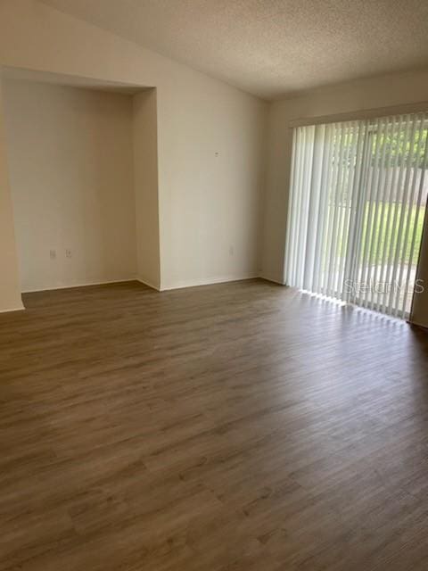 empty room featuring dark wood-type flooring, a textured ceiling, and lofted ceiling