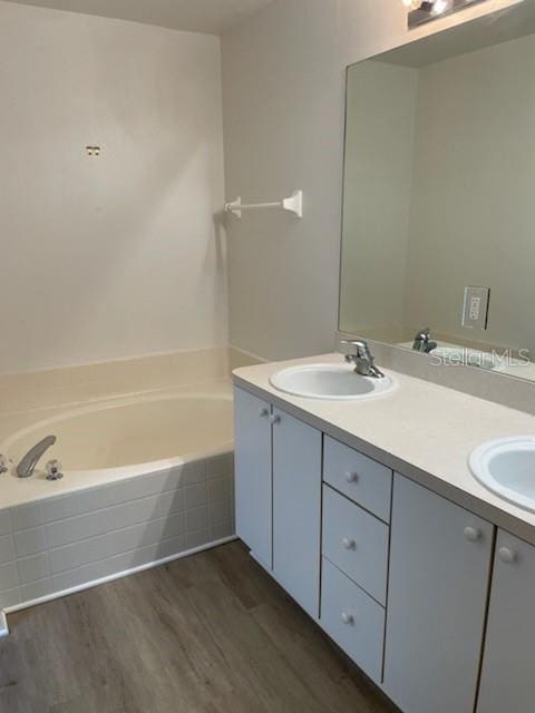 bathroom with a relaxing tiled bath, double vanity, and wood-type flooring