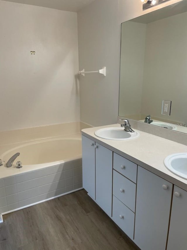 full bath featuring double vanity, a bath, a sink, and wood finished floors