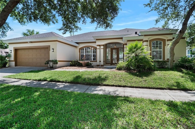 view of front of home featuring french doors, stucco siding, a garage, driveway, and a front lawn