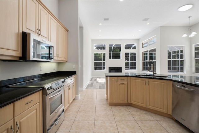 kitchen featuring dark countertops, appliances with stainless steel finishes, a healthy amount of sunlight, light brown cabinets, and a sink