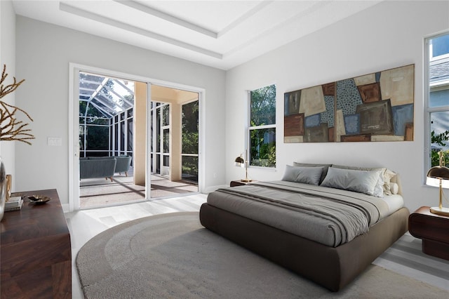 bedroom with access to outside, a tray ceiling, multiple windows, and a sunroom