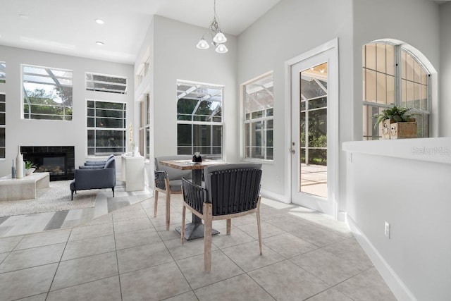 interior space with baseboards, a glass covered fireplace, a notable chandelier, and tile patterned floors