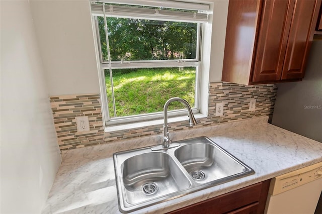 kitchen featuring backsplash, dishwasher, sink, and light stone countertops