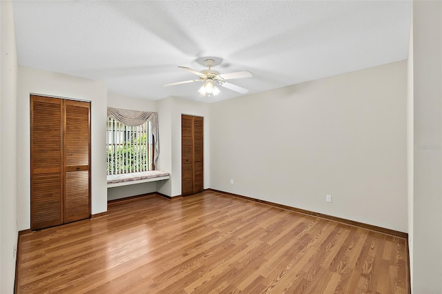 unfurnished bedroom featuring multiple closets, ceiling fan, a textured ceiling, and light wood-type flooring