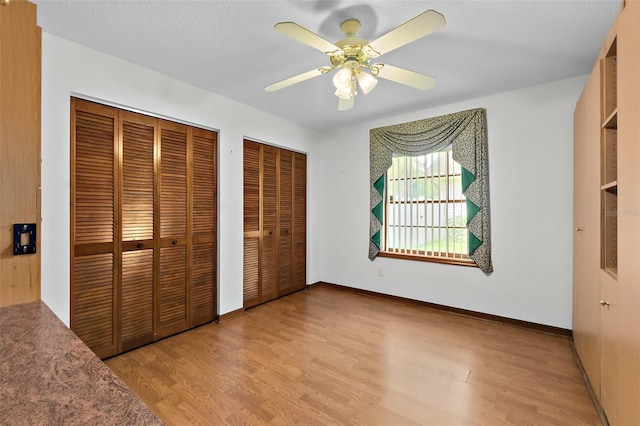 unfurnished bedroom with ceiling fan, a textured ceiling, multiple closets, and light wood-type flooring