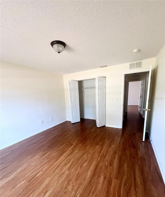 unfurnished bedroom with dark wood-type flooring, a textured ceiling, and a closet