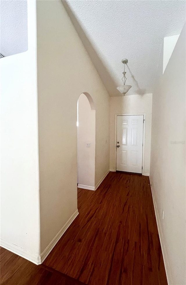 hallway featuring a textured ceiling, hardwood / wood-style flooring, and lofted ceiling