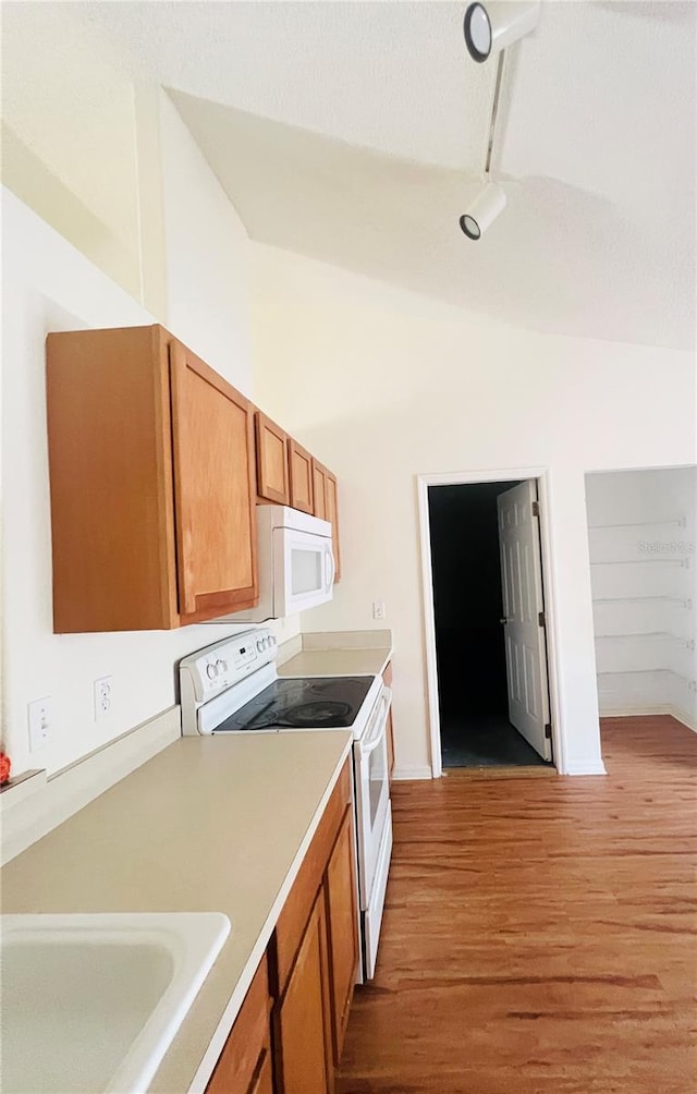 kitchen featuring white appliances, light wood-type flooring, track lighting, vaulted ceiling, and sink