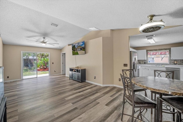 dining room with ceiling fan, vaulted ceiling, a textured ceiling, and hardwood / wood-style floors