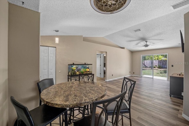 dining space with a textured ceiling, vaulted ceiling, ceiling fan, and light hardwood / wood-style flooring