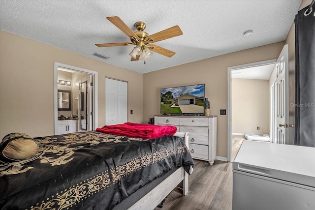 bedroom with a textured ceiling, hardwood / wood-style flooring, connected bathroom, and ceiling fan