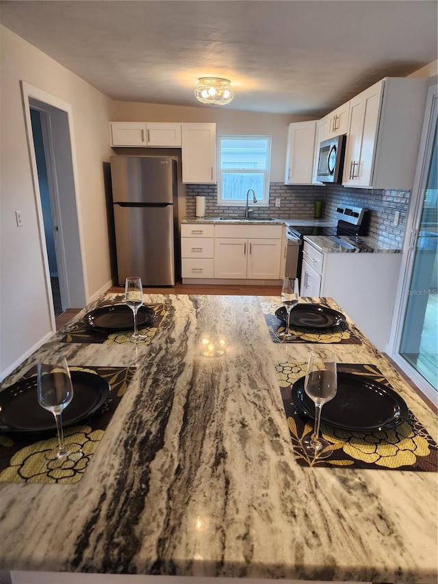 kitchen featuring light stone countertops, sink, backsplash, white cabinets, and appliances with stainless steel finishes