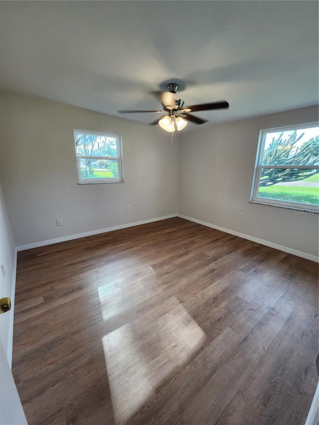 empty room with plenty of natural light, dark wood-type flooring, and ceiling fan