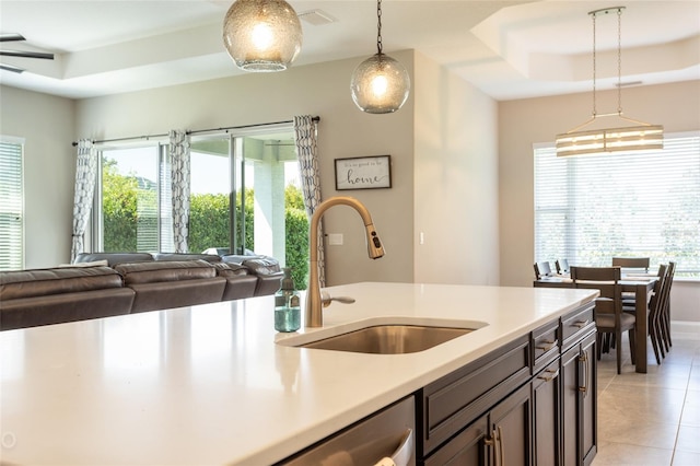 kitchen featuring dark brown cabinets, a tray ceiling, sink, light tile patterned floors, and decorative light fixtures