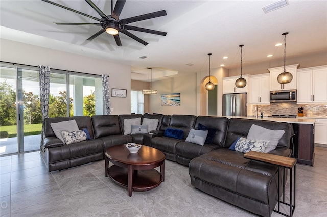 living room with a raised ceiling, ceiling fan, and sink