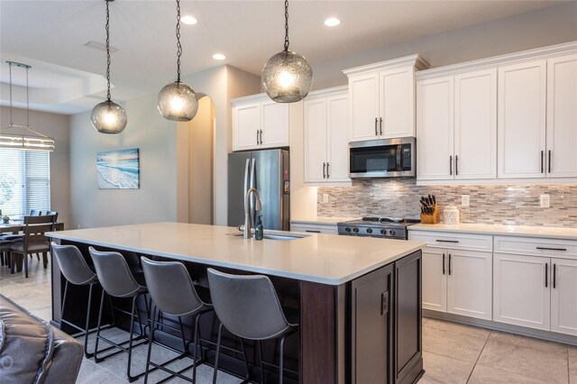 kitchen featuring decorative backsplash, white cabinetry, an island with sink, and appliances with stainless steel finishes