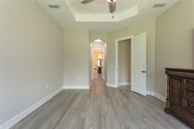 unfurnished bedroom featuring a raised ceiling, ceiling fan, and light hardwood / wood-style floors