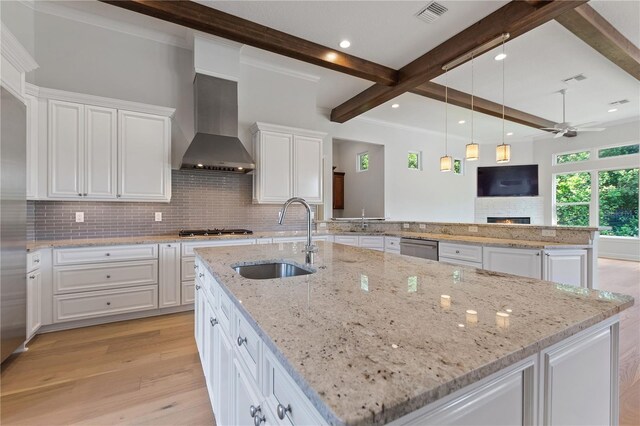 12245 Park Ave, Windermere, FL 34786 - kitchen featuring a sink, wall chimney exhaust hood, ceiling fan, a warm lit fireplace, and light wood finished floors