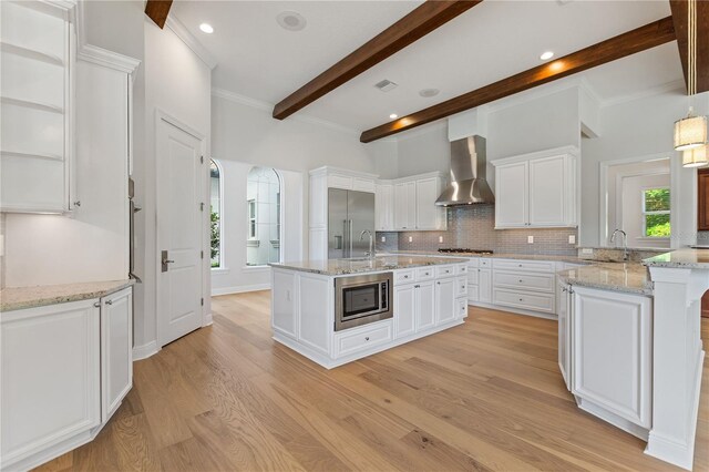 12245 Park Ave, Windermere, FL 34786 - kitchen with wall chimney exhaust hood, built in appliances, beam ceiling, plenty of natural light, and light wood-style floors
