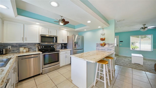 kitchen featuring tasteful backsplash, stainless steel appliances, white cabinetry, ceiling fan, and a raised ceiling