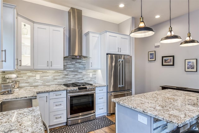 kitchen featuring appliances with stainless steel finishes, tasteful backsplash, wall chimney exhaust hood, decorative light fixtures, and white cabinetry