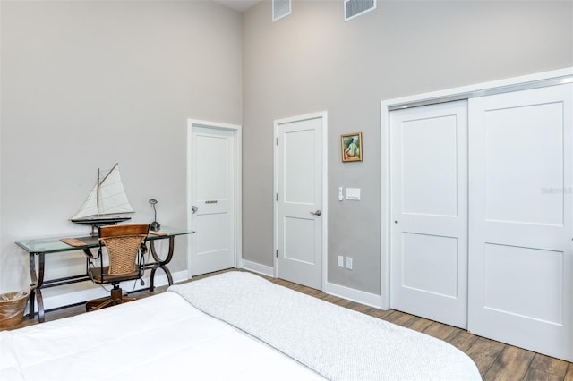 bedroom with wood-type flooring, a towering ceiling, and a closet