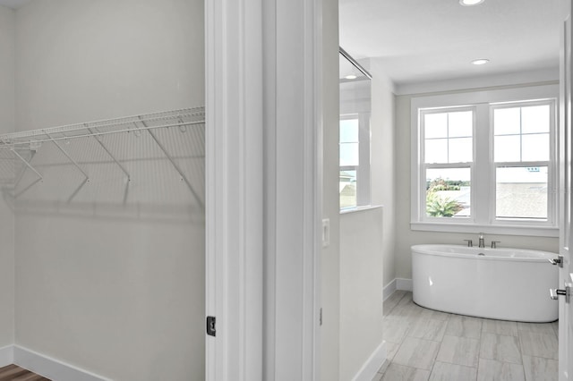 full bath with a freestanding bath, a spacious closet, recessed lighting, and baseboards