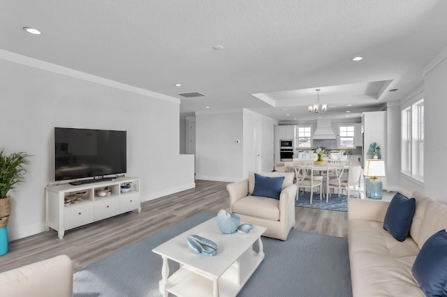 living room with a notable chandelier, wood finished floors, visible vents, baseboards, and a raised ceiling