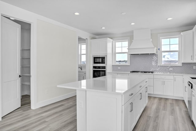 kitchen with gas cooktop, stainless steel oven, light countertops, custom exhaust hood, and a center island