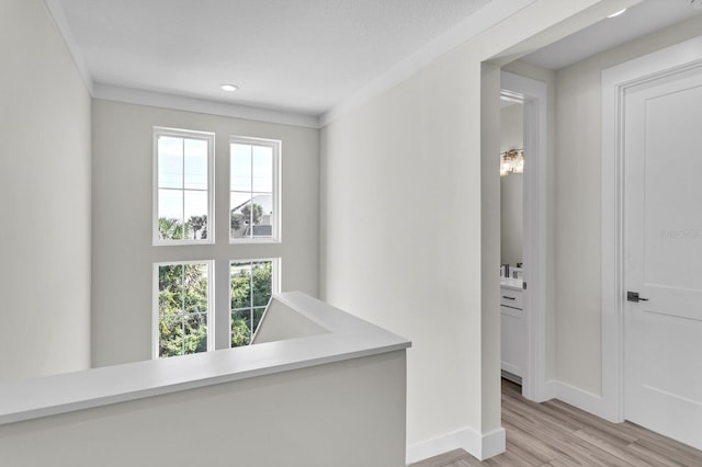 hall with a healthy amount of sunlight, light wood finished floors, baseboards, and crown molding