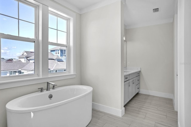 bathroom with a freestanding tub, visible vents, vanity, and baseboards