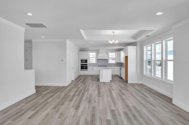 kitchen with custom exhaust hood, visible vents, open floor plan, white cabinets, and oven