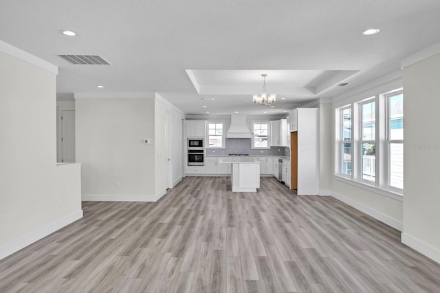 kitchen featuring visible vents, stainless steel oven, open floor plan, white cabinets, and custom range hood