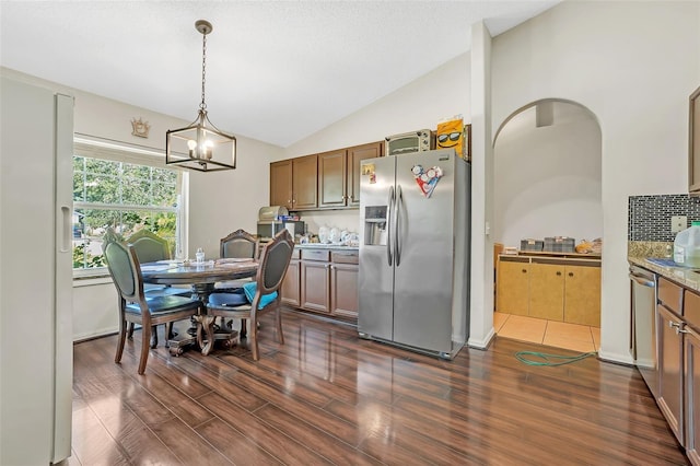 kitchen with dark tile patterned floors, stainless steel appliances, vaulted ceiling, hanging light fixtures, and a notable chandelier