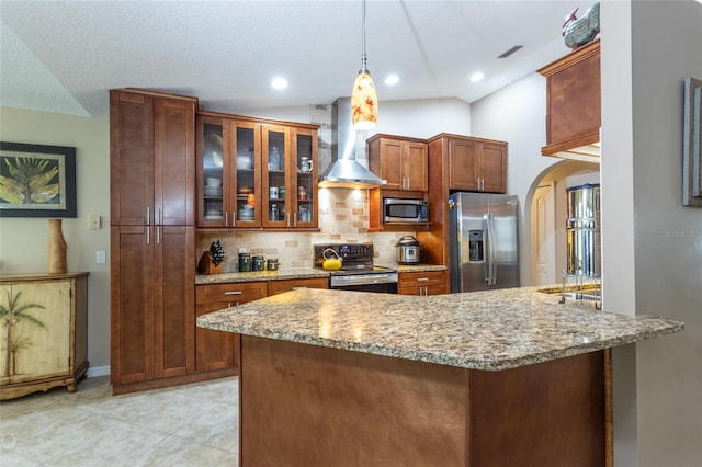 kitchen with light stone countertops, vaulted ceiling, appliances with stainless steel finishes, wall chimney exhaust hood, and pendant lighting