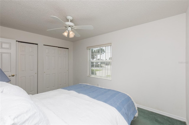 carpeted bedroom featuring two closets, a textured ceiling, and ceiling fan