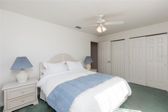 bedroom featuring ceiling fan, dark carpet, a textured ceiling, and two closets