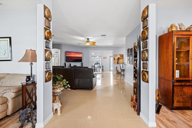 living room with a textured ceiling, ceiling fan, and wood-type flooring