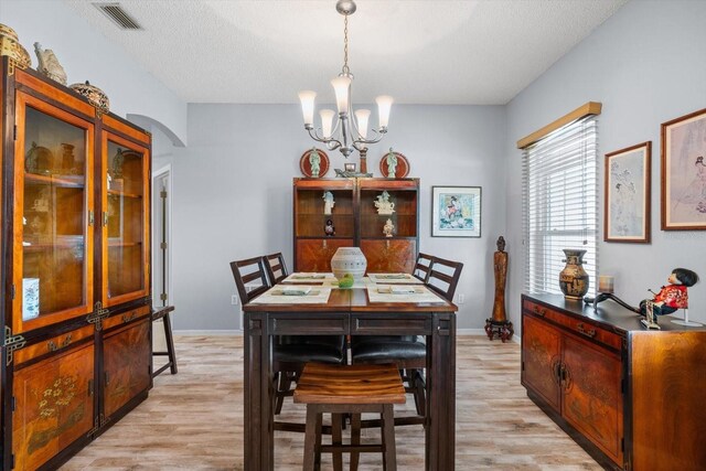 dining space with a notable chandelier, light wood-type flooring, and a textured ceiling